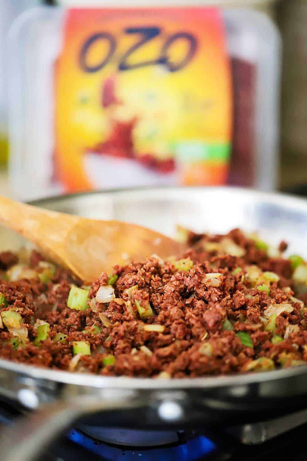 A stainless steel skillet filled with ground plant-based protein and sautéd vegetables in front of a package of OZO plant-based protein. 