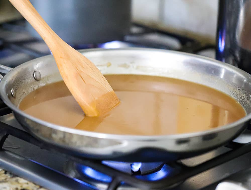 A large stainless steel skillet filled with brown gravy with a wooden spoon in it.