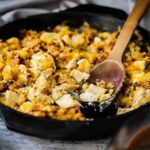 A large black cast-iron skillet filled with turkey and stuffing dressing with some of the food scooped out.