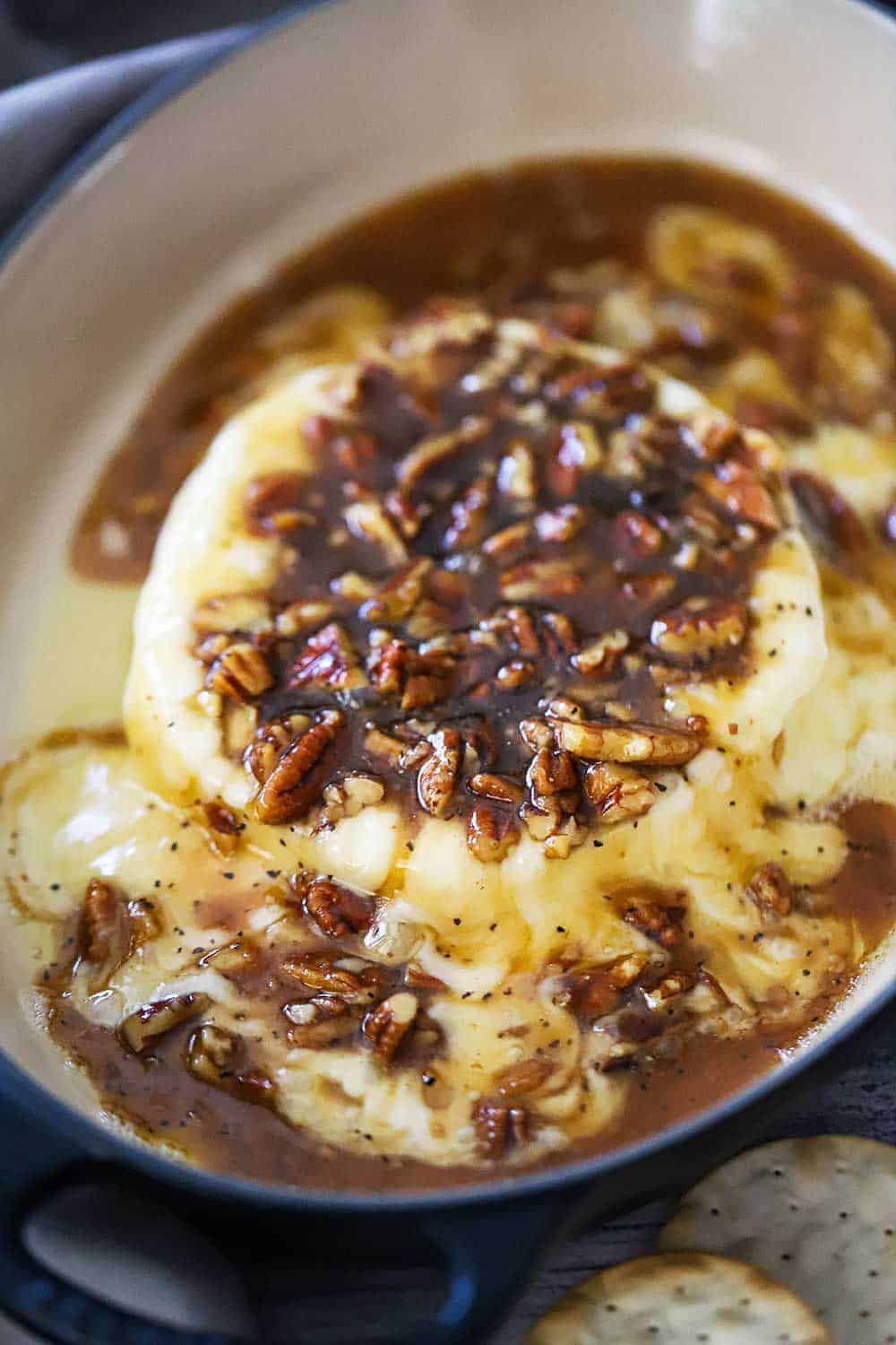 A wheel of baked brie in a baking dish smothered in pecan praline sauce. 