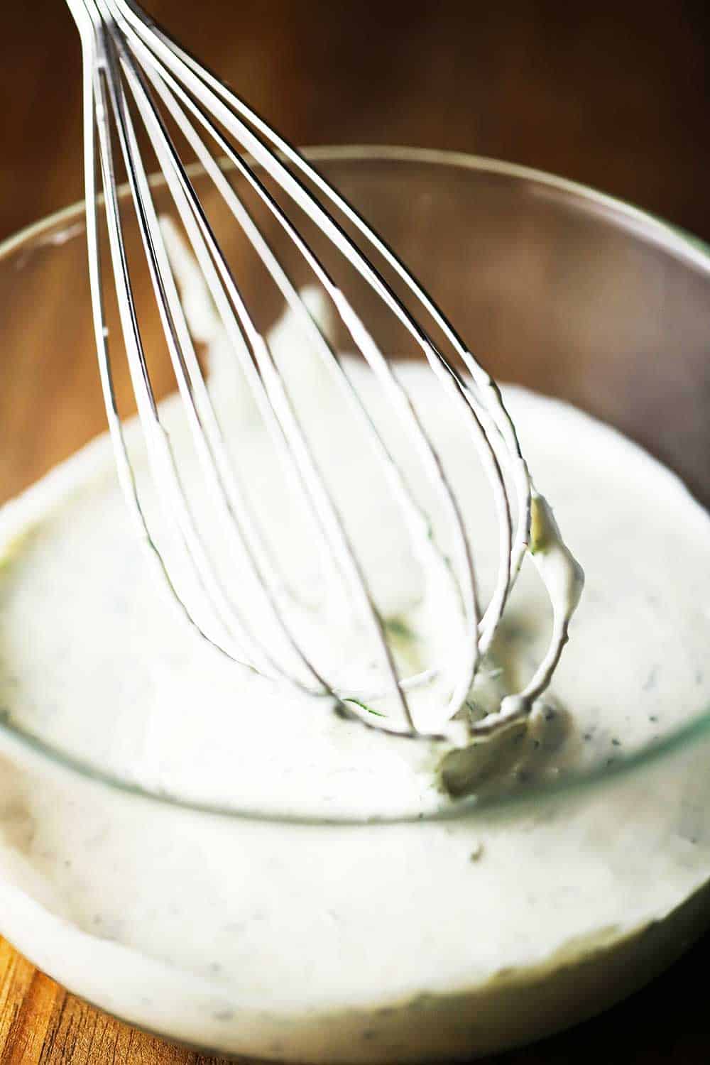 A medium-sized glass bowl filled with a creamy horseradish sauce with a whisk in it. 