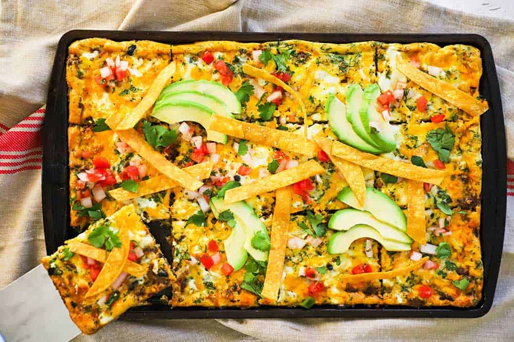 A fully cooked sheet-pan Mexican frittata with a person removing a slice with a spatula. 