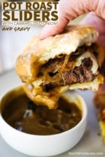 A hand holding a pot roast slider that has been dipped in gravy with a bite taken out of it.