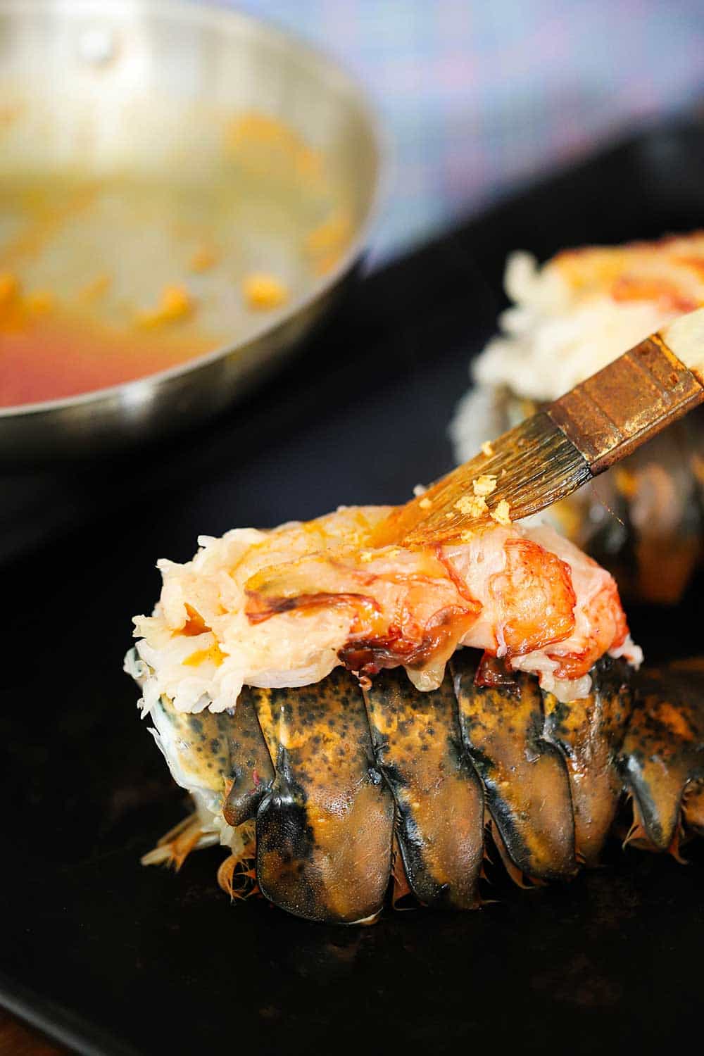 A person brushing melted butter with paprika onto the exposed flesh of a lobster sitting on top of the tail. 