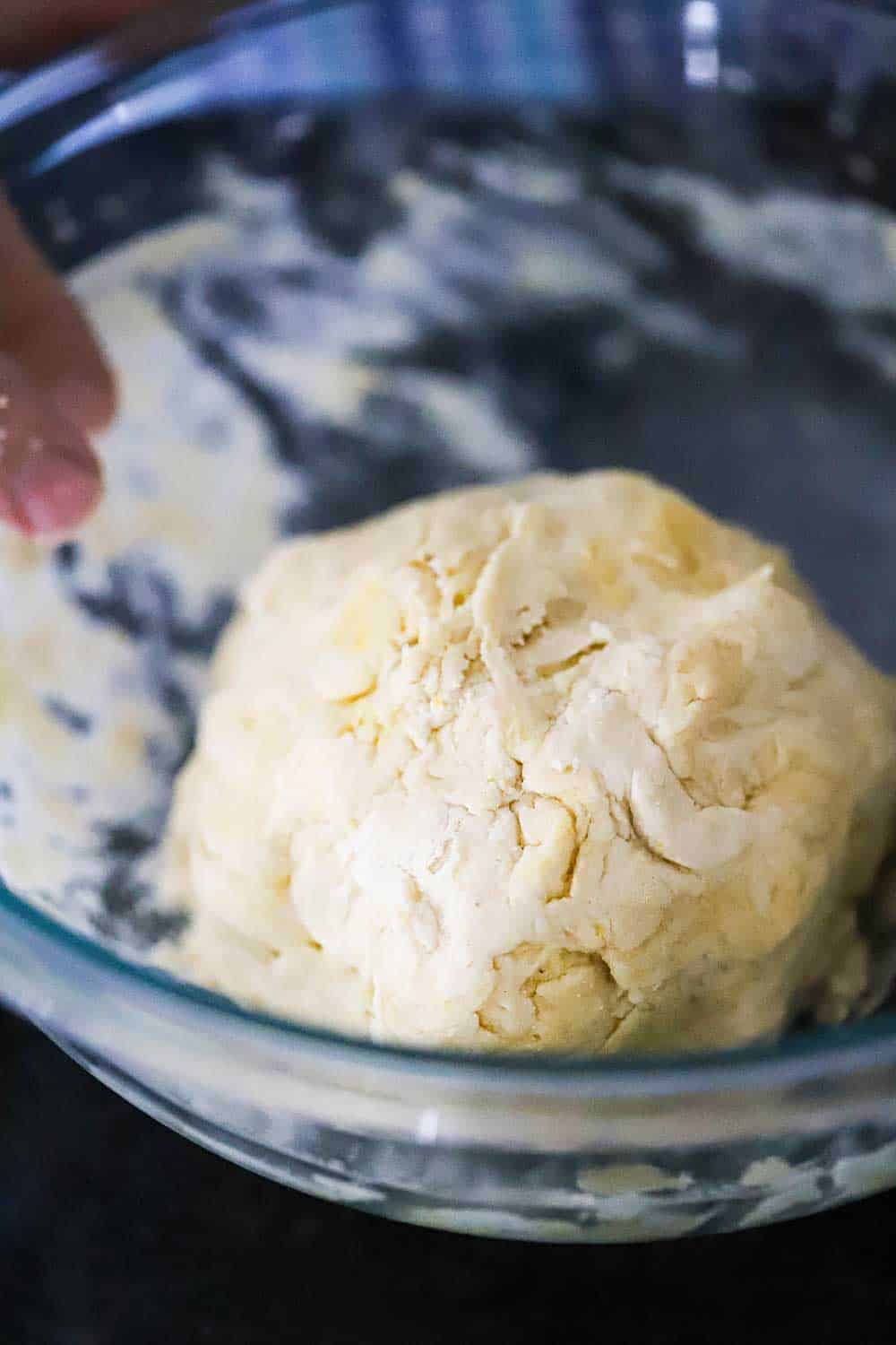 A flakey ball of pizza dough in a glass bowl with wet flour on the sides of the vessel. 