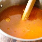Shellfish stock in a large stock pan with a wooden spoon submerged into the liquid.