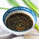A small colorful Asian bowl filled with hot and sweet dipping sauce next to several scallions.