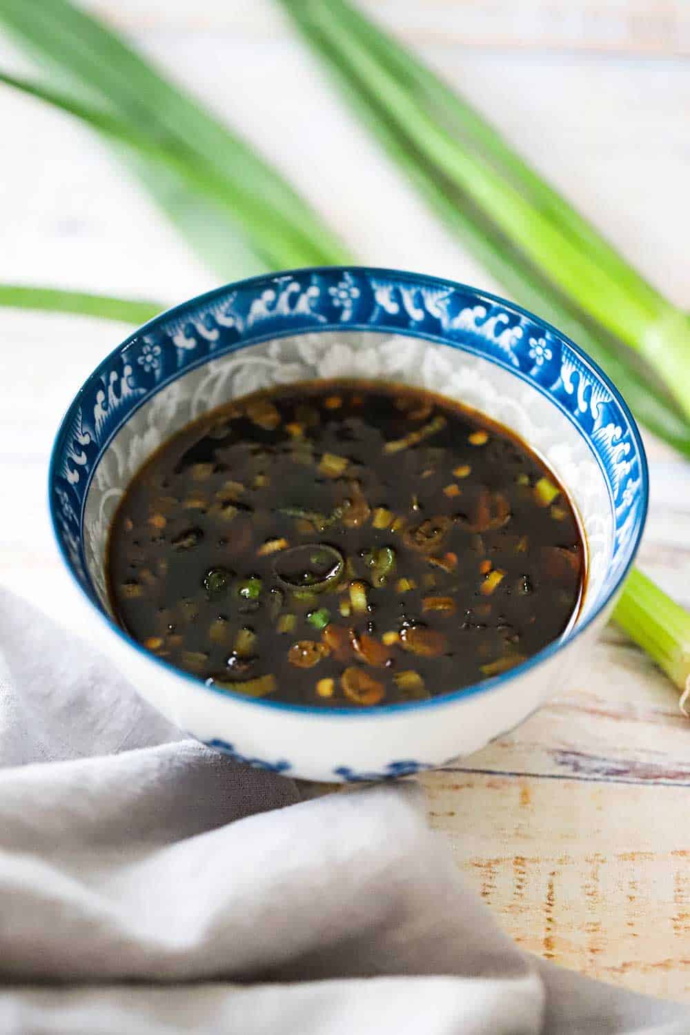 A small colorful Asian bowl filled with hot and sweet dipping sauce next to several scallions. 