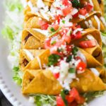 A row of cooked flautas on a bed of shredded lettuce all on a white oval platter.