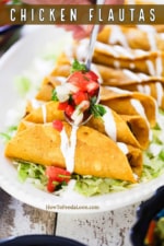 A person spooning fresh pico de gallo down the center of a line of chicken flautas on a platter lined with shredded lettuce.