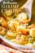 Shrimp curry being stirred in a large stainless steel skillet.