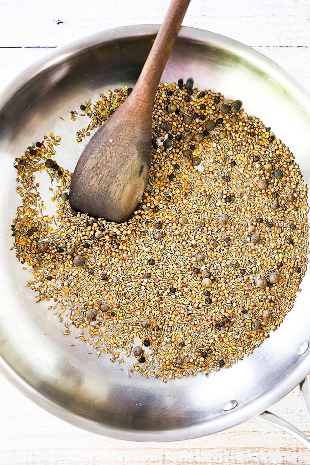A large silver skillet filled with various seeds with a wooden spoon inserted into them. 