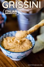 A breadstick that has been plunged into a bowl of hummus and being held just over the top of the dip.