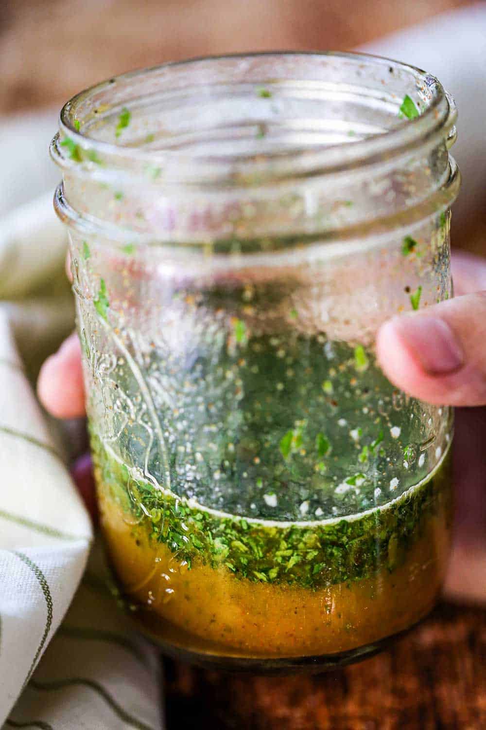 A hand holding a glass jar half filled with cilantro lime dressing.
