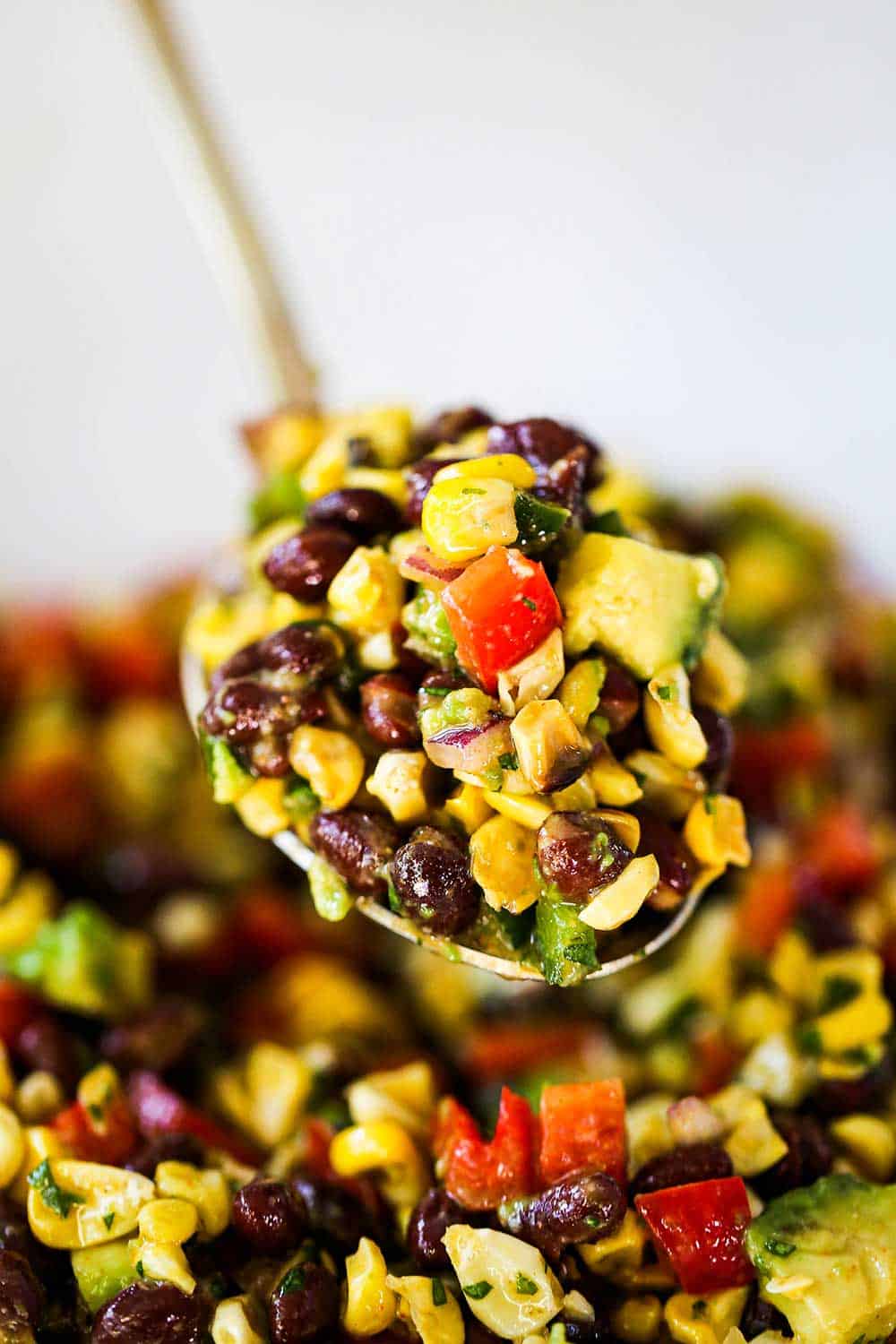 A large gold serving spoon holding up a big scoop of black bean and corn salad.