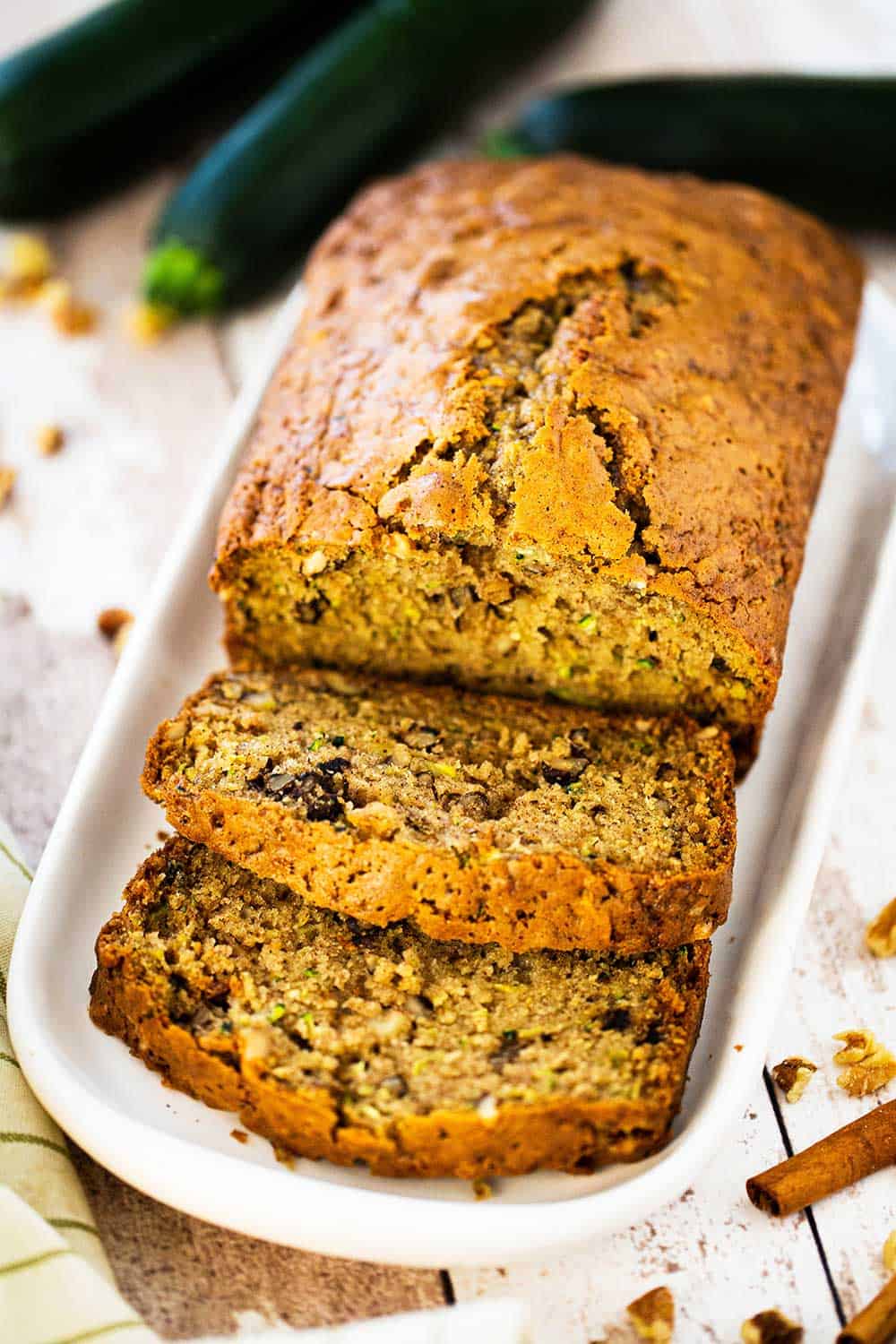 A loaf of freshly baked zucchini bread that has a couple of slices cut on an small platter. 