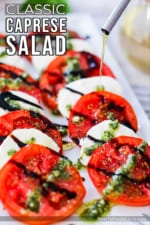 A thin drizzle of olive oil being poured from an olive oil dispenser onto a platter filled with caprese salad.