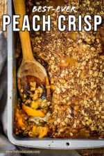 A silver baking pan filled with fully baked peach crisp with a wooden spoon inserted in the side.