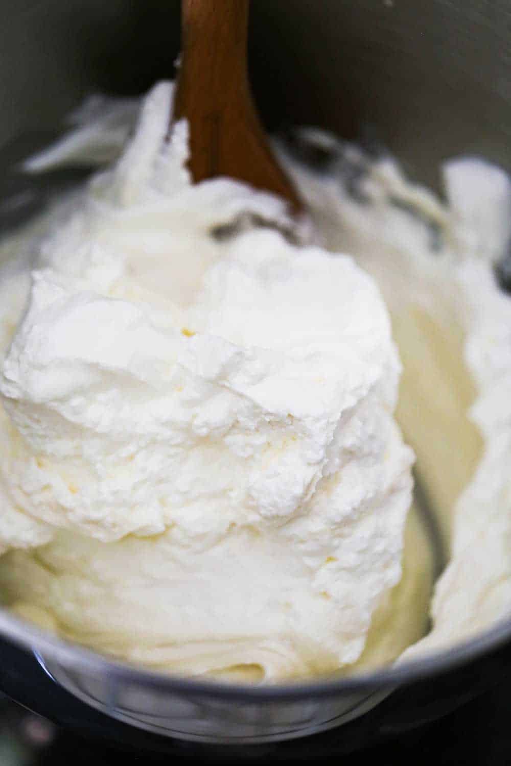 A mixing bowl filled with a white cream filling that is being held up with a wooden spoon.