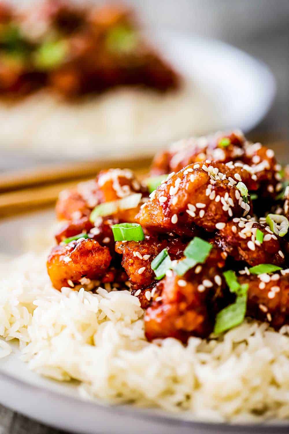 A close-up view of plate filled with sesame chicken on top of a bed of rice.