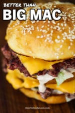 A homemade Big Mac hamburger sitting on a cutting board with Russian dressing dripping from one of the patties.