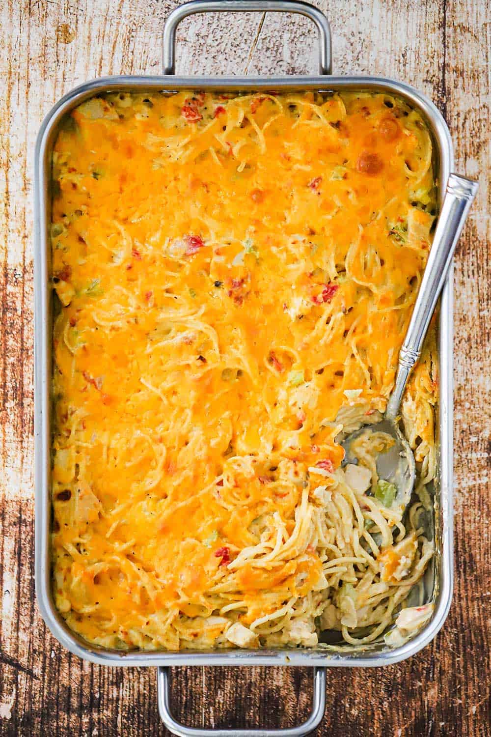A large lasagna pan filled with chicken spaghetti with a small portion of the dish removed in one corner with a serving spoon stuck in the dish. 