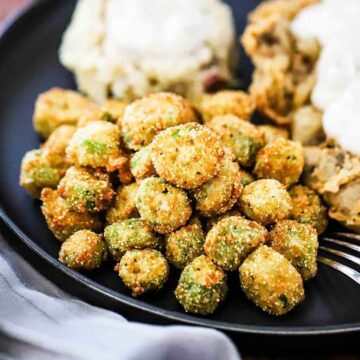 A blue dinner plate willed with chicken fried steak, mashed potatoes, both topped with gravy, all next to a pile of fried okra.
