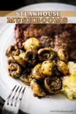 A white dinner plate filled with a grilled steak sitting next to a pile of sautéed whole mushrooms.