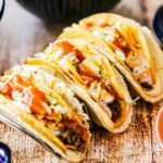 Three cheesy gordita crunch tacos sitting on a taco holder on a wooden surface.