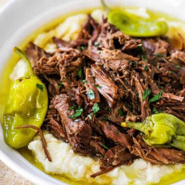A white bowl filled with mashed potatoes topped with Mississippi pot roast.