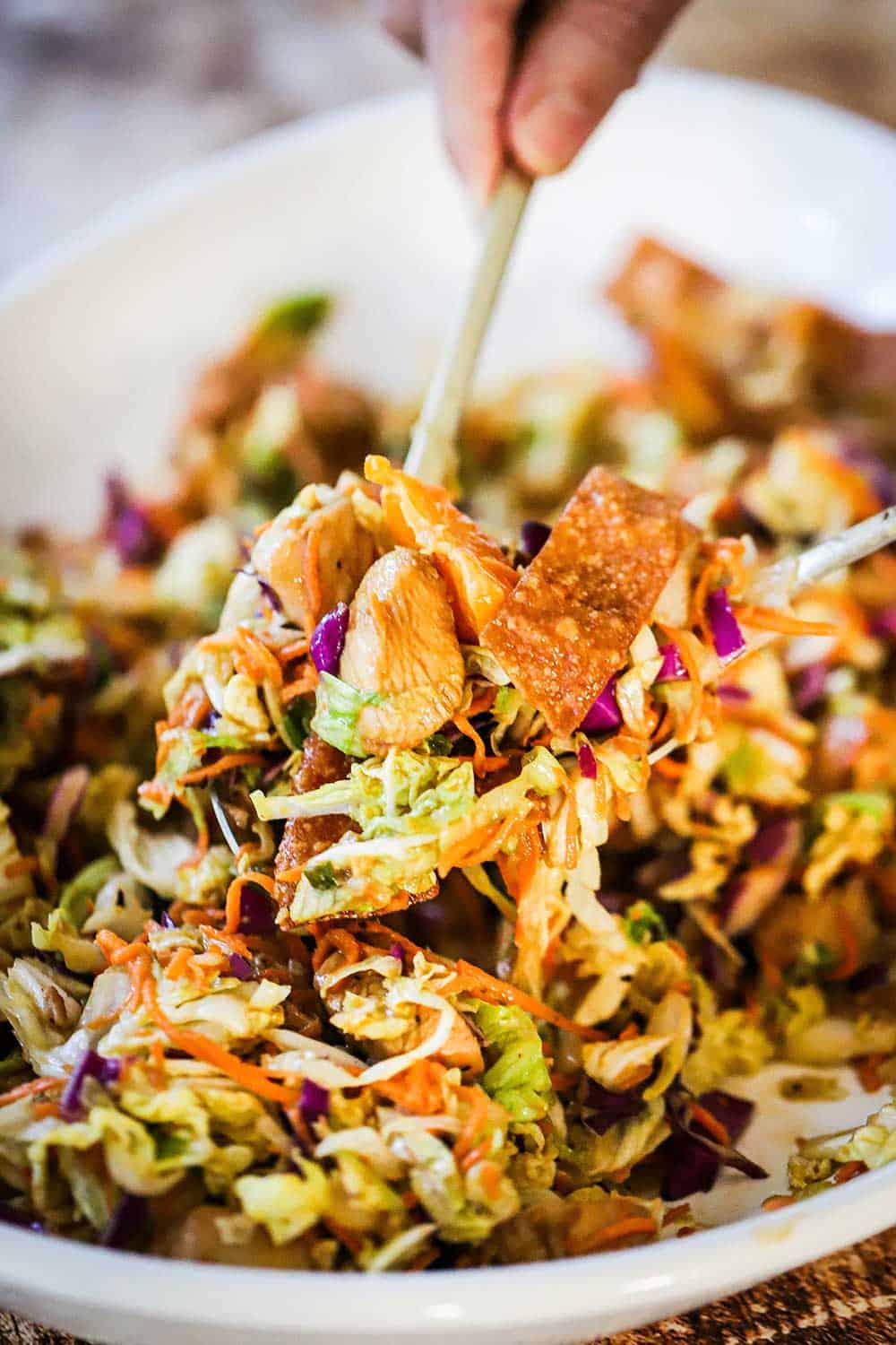 A large serving spoon scooping up a helping of Chinese chicken salad over a platter of the same. 