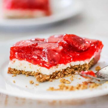A slice of strawberry pretzel salad with a bite taken out of it sitting on a white plate with a fork next to it.
