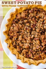 A sweet potato pie in a pie crust with fluted edges sitting in a white pie dish on an autumnal place setting.