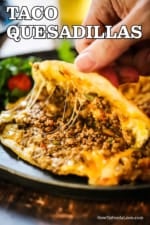 A person using his fingers to open a taco quesadilla filled with beef taco meat and melted gooey cheese.