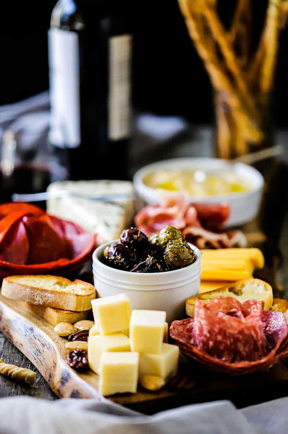 A charcuterie board filled with cubed cheeses, meats in the shape of a flower, bread sticks, and a bowl of hummus. 