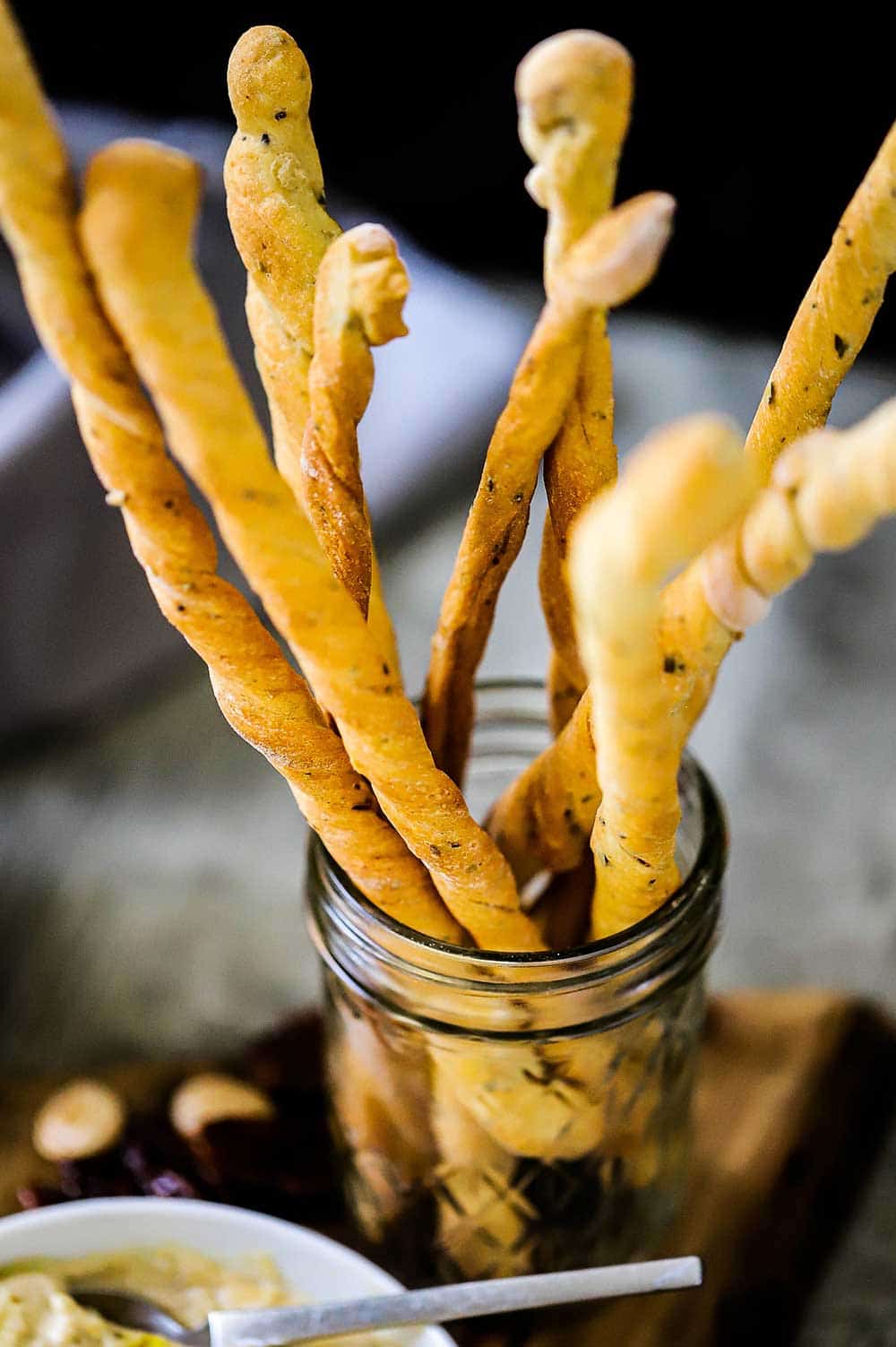 A small glass jar filled with tall grissini, also known as Italian breadsticks. 