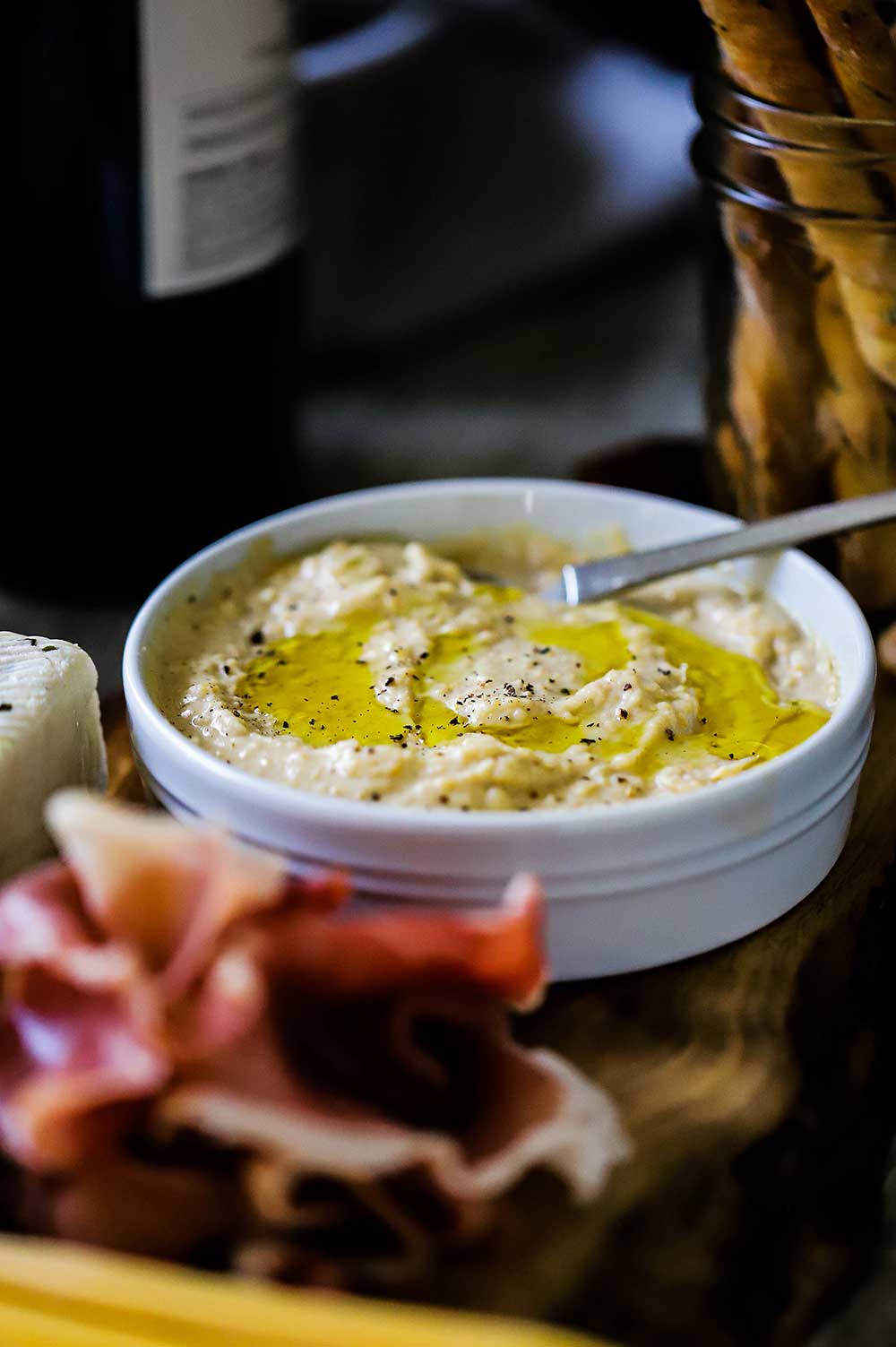 A small white bowl filled with homemade hummus topped with olive oil and ground black pepper. 