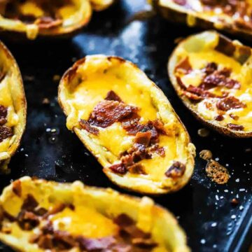 A black baking sheet filled with loaded potato skins.