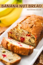 A loaf of banana nut bread with a couple of slices cut sitting on a white serving dish.
