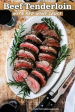An oval white serving platter filled with slices of beef tenderloin with fresh rosemary along the edges of the dish.