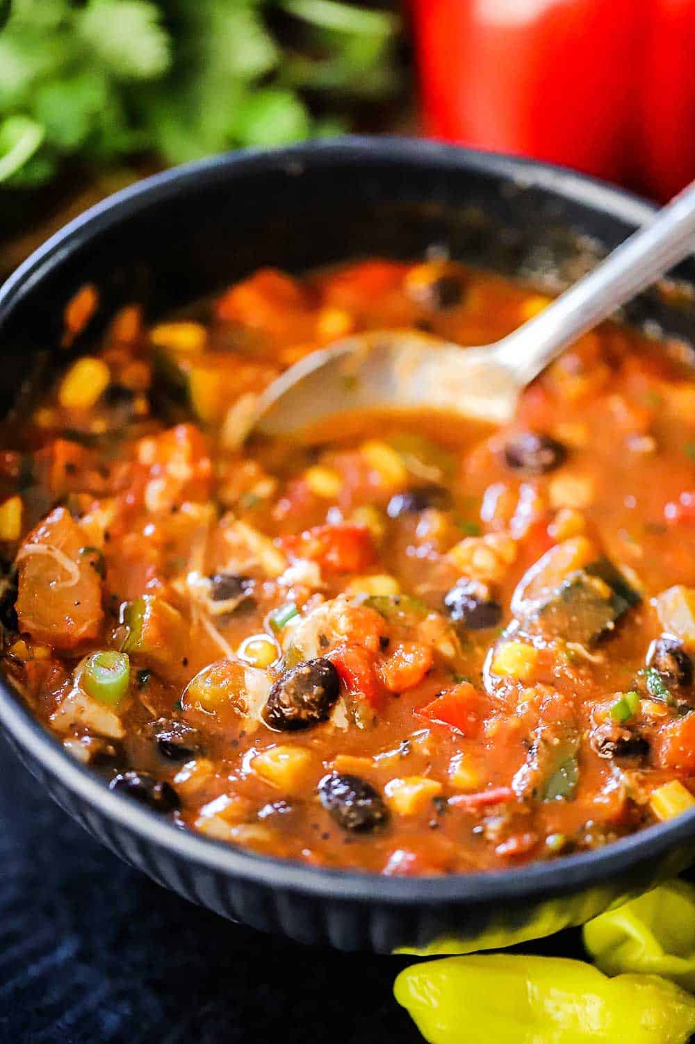 A bowl filled with vegetable chili with black beans and a spoon inserted into it.