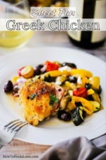 A white dinner plate filled with Sheet Pan Greek Chicken next to a glass of white wine.