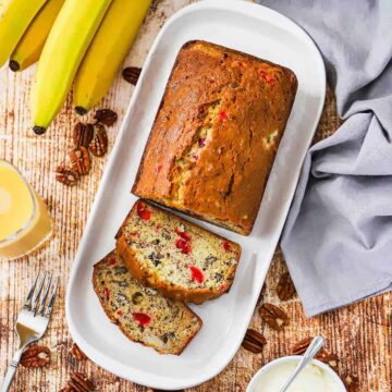 A loaf of banana nut bread with a couple slices that have been cut on a rectangular white serving dish.