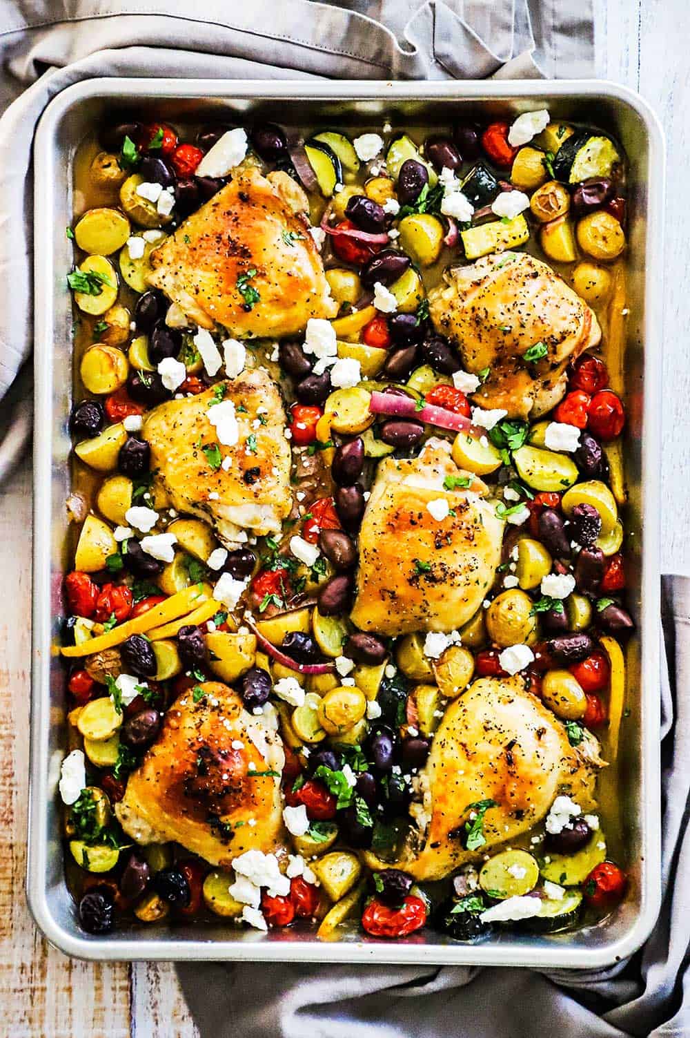 Sheet Pan Greek Chicken fully cooked with vegetables and feta cheese sprinkled all over the top. 