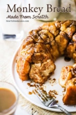 Homemade monkey bread with a few pieces missing on a white round platter next to a glass cup of coffee.