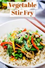 A white circular plate filled with vegetable stir-fry with brown chop sticks sitting on the side of the bowl.