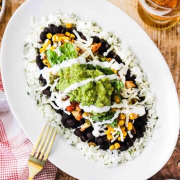 A chicken burrito bowl pile high in a white oval dish with a gold fork next to it.