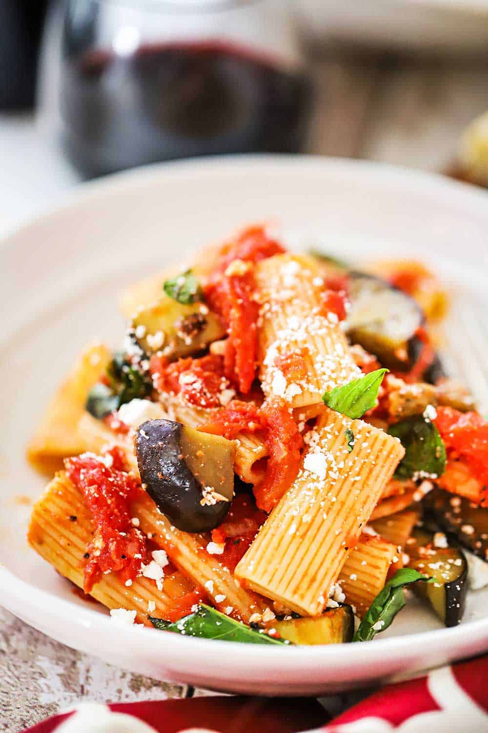 A white dinner bowl filled with a pile of Pasta alla Norma topped with crumbled cheese.