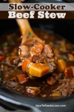A wooden spoon being lifted out of a slow-cooker filled with beef stew.