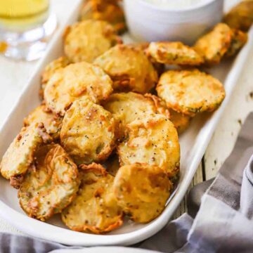 A rectangular platter filled with crispy fried pickles stack on top of each other.